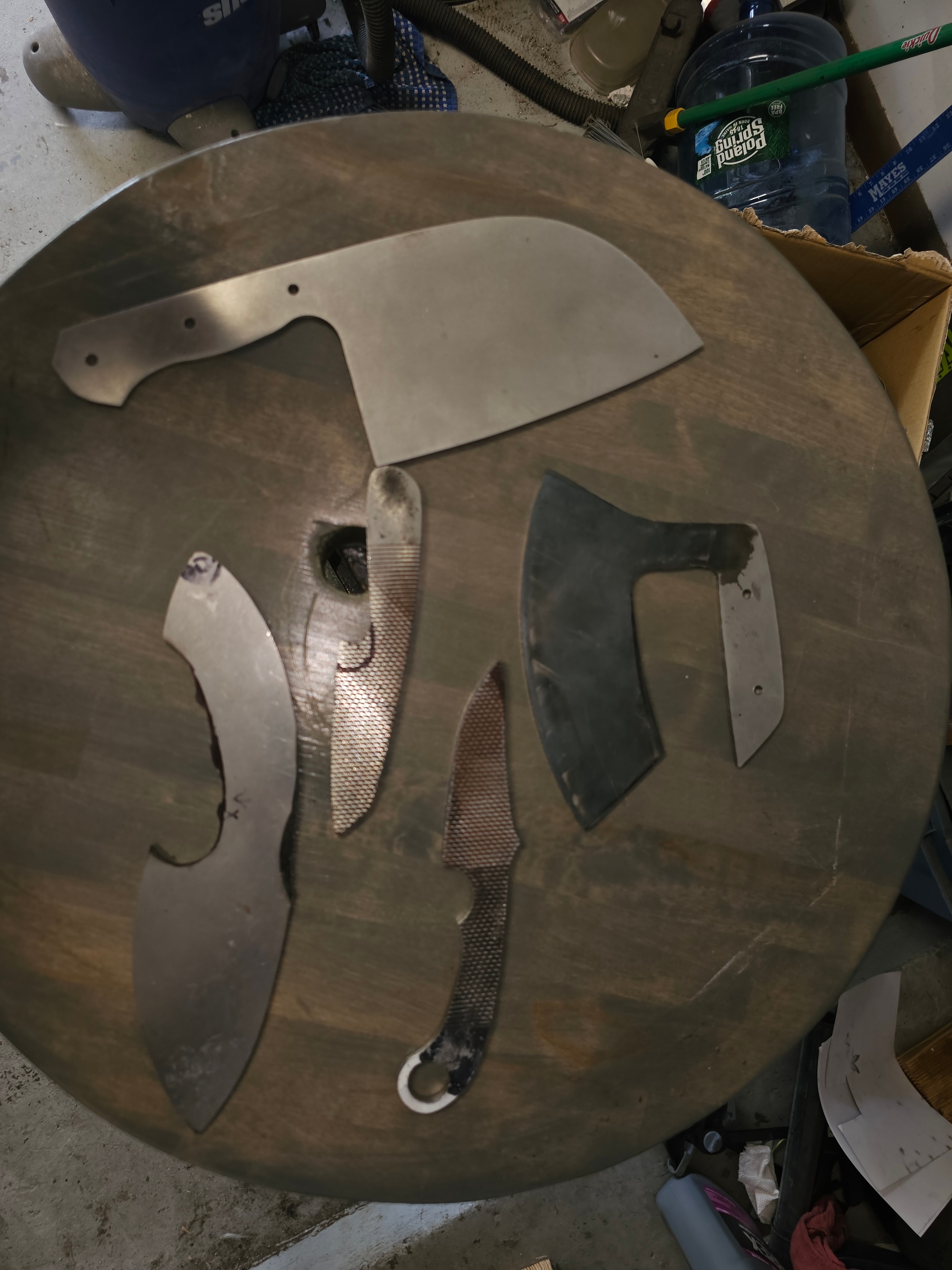 Collection of custom knife and axe blades displayed on round wooden board