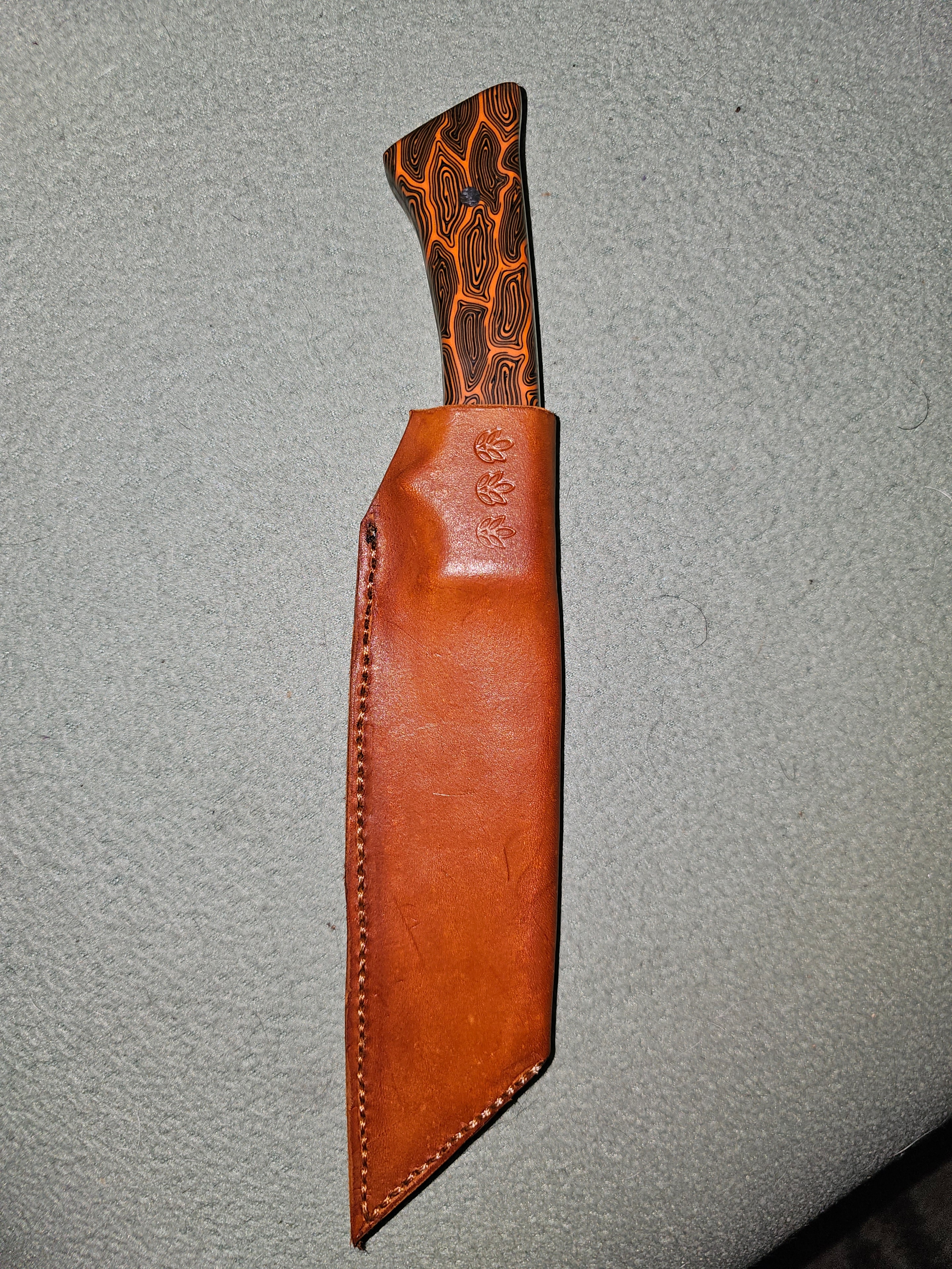 Custom knife with orange and black micarta handle in leather sheath